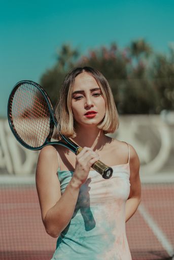 A shallow focus of a confident female with hair highlights holding a tennis racquet and posing at a court