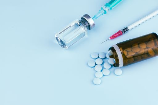 A closeup of pills and a container with a syringe on blue background