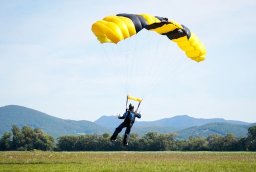 A closeup of a man parachuting near the ground with a yellow parachute during daylight