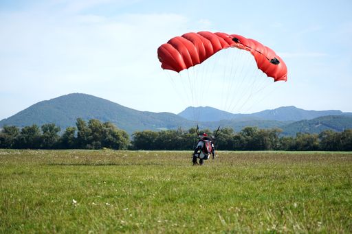 A closeup of a man parachuting near the ground with a red parachute during daylight
