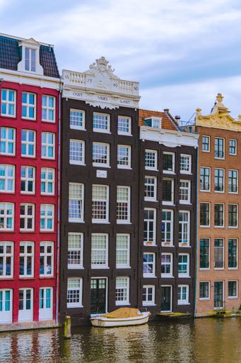 A vertical shot of Damrak avenue buildings with a boat in a canal, Amsterdam, the Netherlands