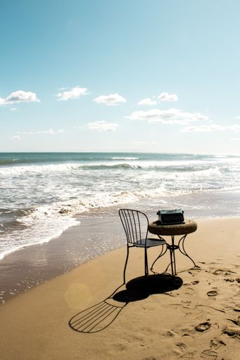 A vertical shot of a steel chair and a small table on the sandy shore on a clear sky background