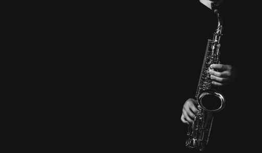 A grayscale shot of a cool and handsome guy playing his saxophone isolated on a dark background