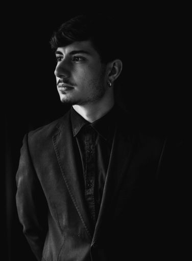 A vertical closeup shot of a handsome guy on a coat and tie isolated on a dark background