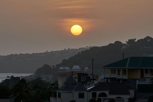 The buildings and mountains covered with trees with an orange sun during sunset in the background