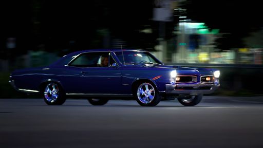 A long exposure shot of a blue Chevrolet Nova car driving at high speed on the road in the evening