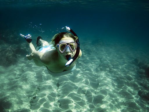 A female diver diving in the sea wearing snorkel goggles and fins