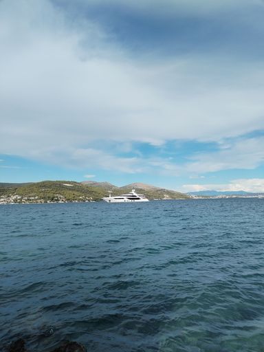 A vertical shot of a seascape with a white yacht on the horizon