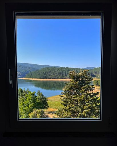 A beautiful scenery of a lake view with blue sky and greenery from a glass window