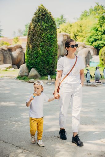 A vertical shot of a stylish young mother holding her sons hand as he eats ice cream in a park