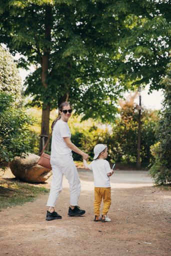 A vertical shot of a stylish young mother holding her sons hand as they walk around in a park