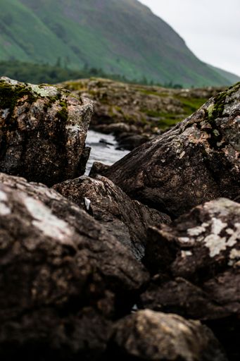 A selective focus shot of the stones in the river, with a green mountain slope in the background