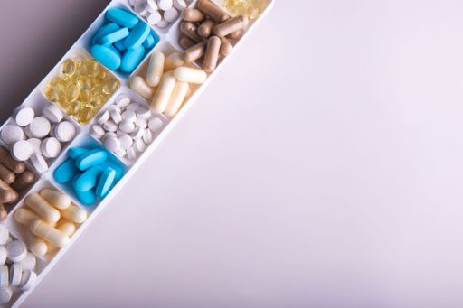 A high-angle shot of blue, yellow, brown, and white oval medicines on a yellow background.