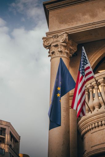 A low angle of the flag of the United States and the flag of Europe swaying on a balcony of a building