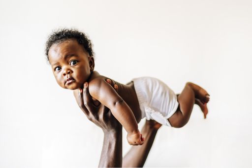 An African-American baby being held up in the air by her parent against a white wall