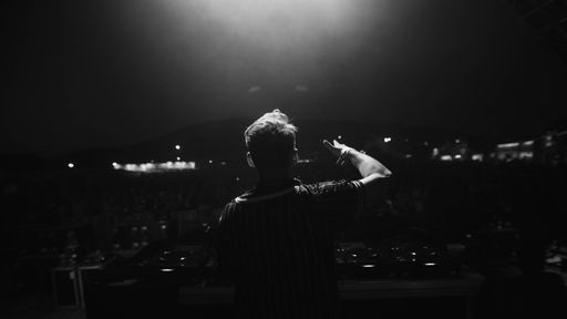 A grayscale back view of a male DJ on a stage