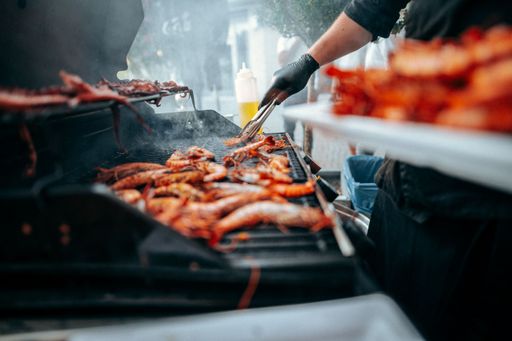 A closeup shot of a cook using tongs to put meat on a grill