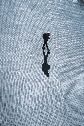 A high angle shot of a pedestrian walking with a shadow on a cobblestone street