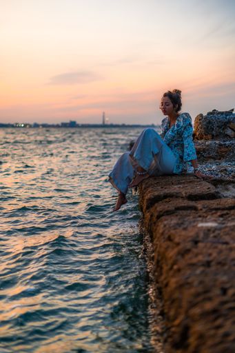 A vertical shot of a young female relaxing on stones surrounded by the sea during a beautiful sunset