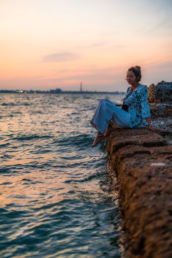 A vertical shot of a young female relaxing on stones surrounded by the sea during a beautiful sunset