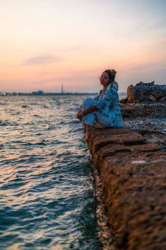 A vertical shot of a young female relaxing on stones surrounded by the sea during a beautiful sunset