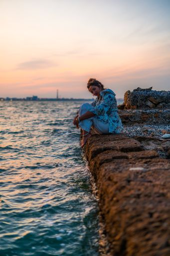 A vertical shot of a young female relaxing on stones surrounded by the sea during a beautiful sunset