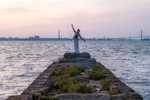 A young female standing on rocks surrounded by the sea in the evening