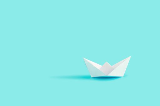 A closeup shot of a white paper boat on the blue background