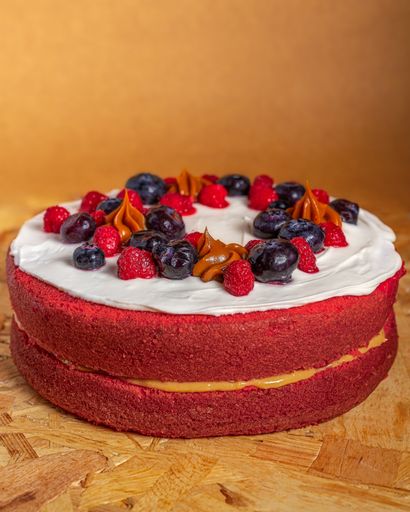 A vertical shot of a delicious red velvet cake decorated with berries on a wooden surface