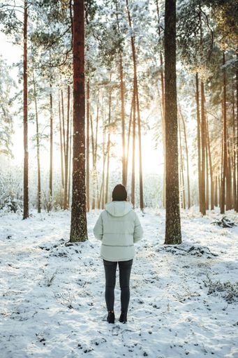 A vertical shot of the woman in a white puffer jacket against the background of snow-covered trees.