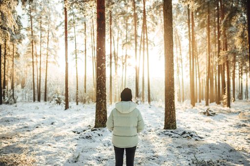 The woman in a white puffer jacket against the background of snow-covered trees on a sunny day.