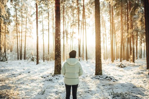 The woman in a white puffer jacket against the background of snow-covered trees on a sunny day.