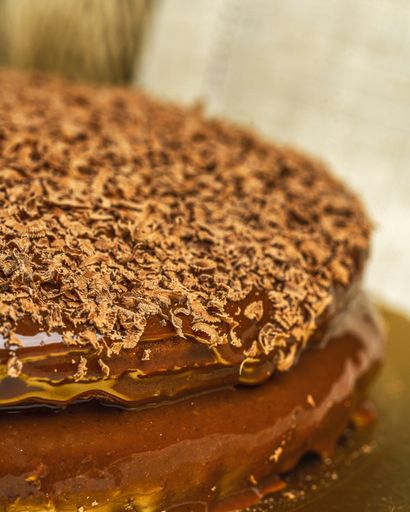A vertical shot of a delicious cake covered in ganache and decorated with chocolate shavings