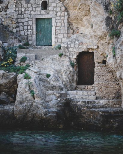 A small arch-shaped doorway in a stone wall located near a body of water surrounded by large rocks