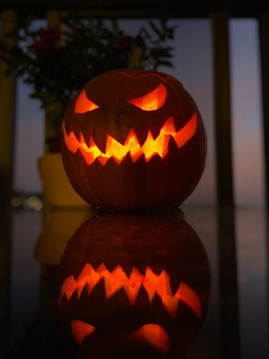 A closeup shot of a lit orange carved Halloween pumpkin