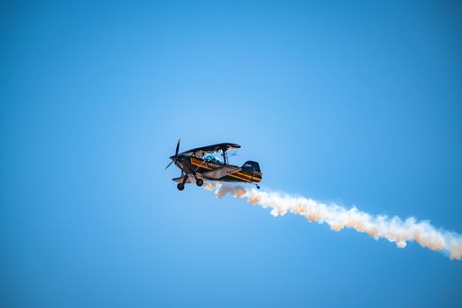 A vintage single-engine plane soaring through the sky, with a long trail of smoke billowing behind it