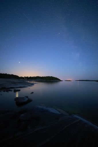 A vertical shot of a lake reflecting the starry sky with trees and a night sky in the background, perfect for wallpapers
