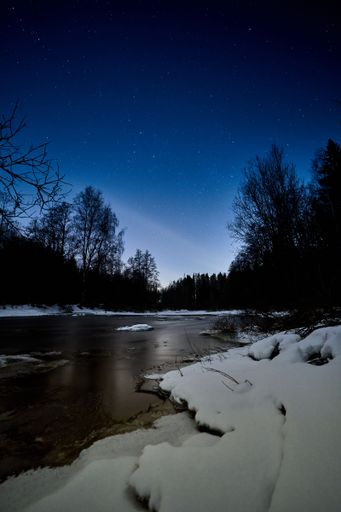 A vertical shot of a small lake at night with a blue starry sky in the background, perfect for wallpapers