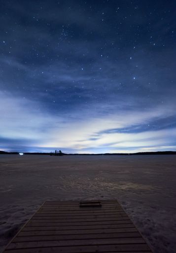 A vertical shot of a wooden boardwalk with a cloudy, starry night sky in the background