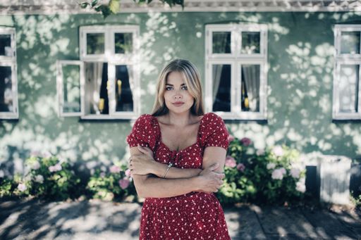 A young blonde female in a red spotted dress posing in front of a house