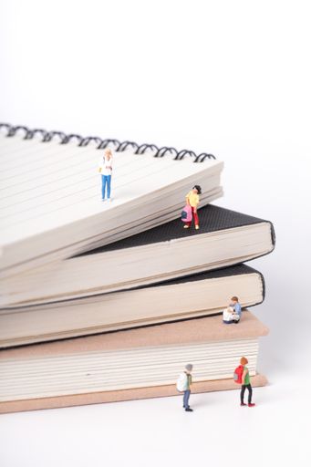 A vertical shot of little figurines of students standing on and around textbooks