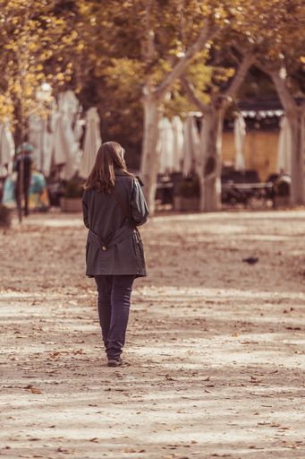 A rear view of a girl walking on fallen autumn leaves in the park