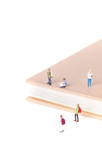 View of little figurines of students standing on and around a textbook on white background