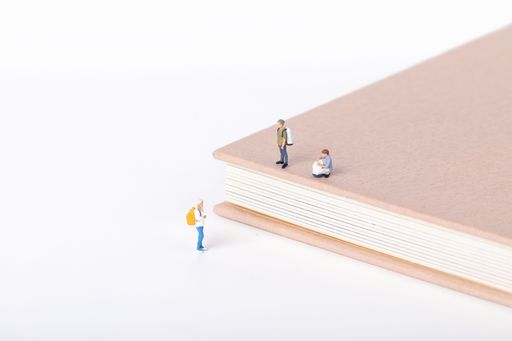 A view of little figurines of students standing on and around a textbook on white background