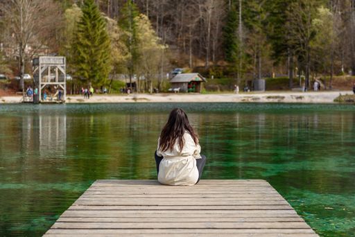 A back shot of a young woman sitting on a wooden pier on the shore of Lake Jasna in Slovenia