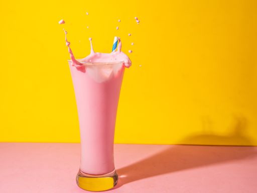A glass of strawberry smoothie isolated on yellow and pink background