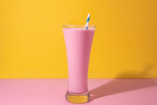 A glass of strawberry smoothie isolated on yellow and pink background