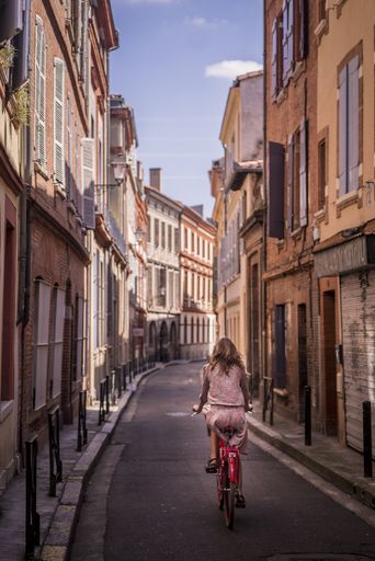 A vertical shot of a female riding a bike in the streets of Toulouse, France