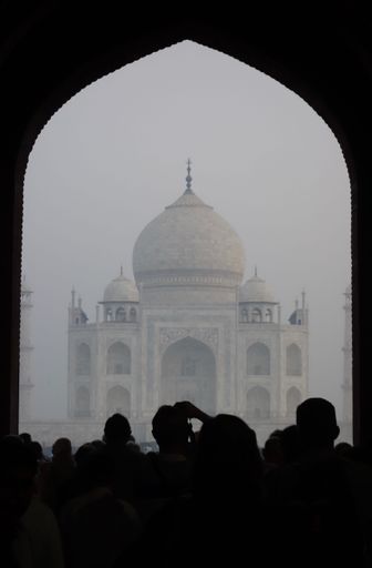 A silhouette shot of people looking at the Taj Mahal in India on a foggy day