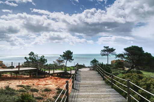 A view of a wooden stairway leading to the coast of Algarve, Portugal, with a blue Atlantic ocean in the background, and sky and clouds on a sunny day